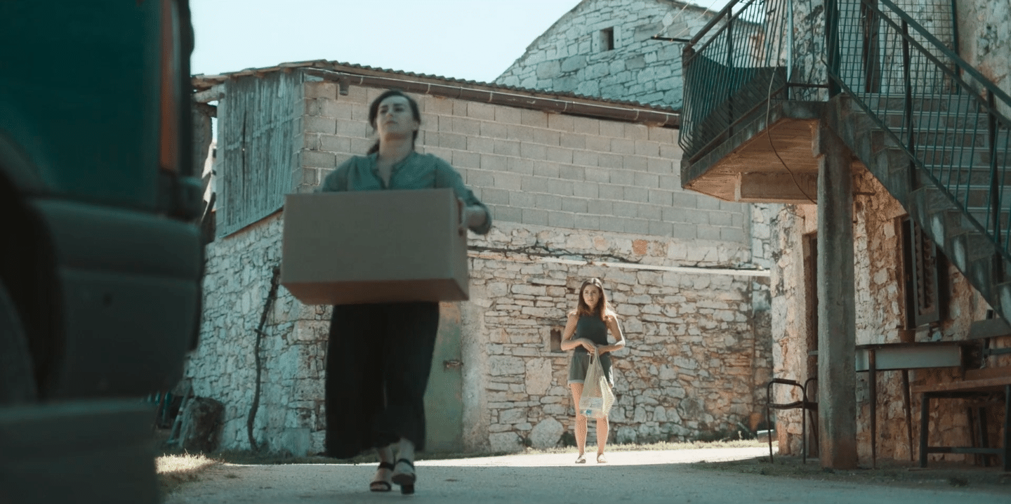 Woman carrying a box in an urban alley with a woman in the background.