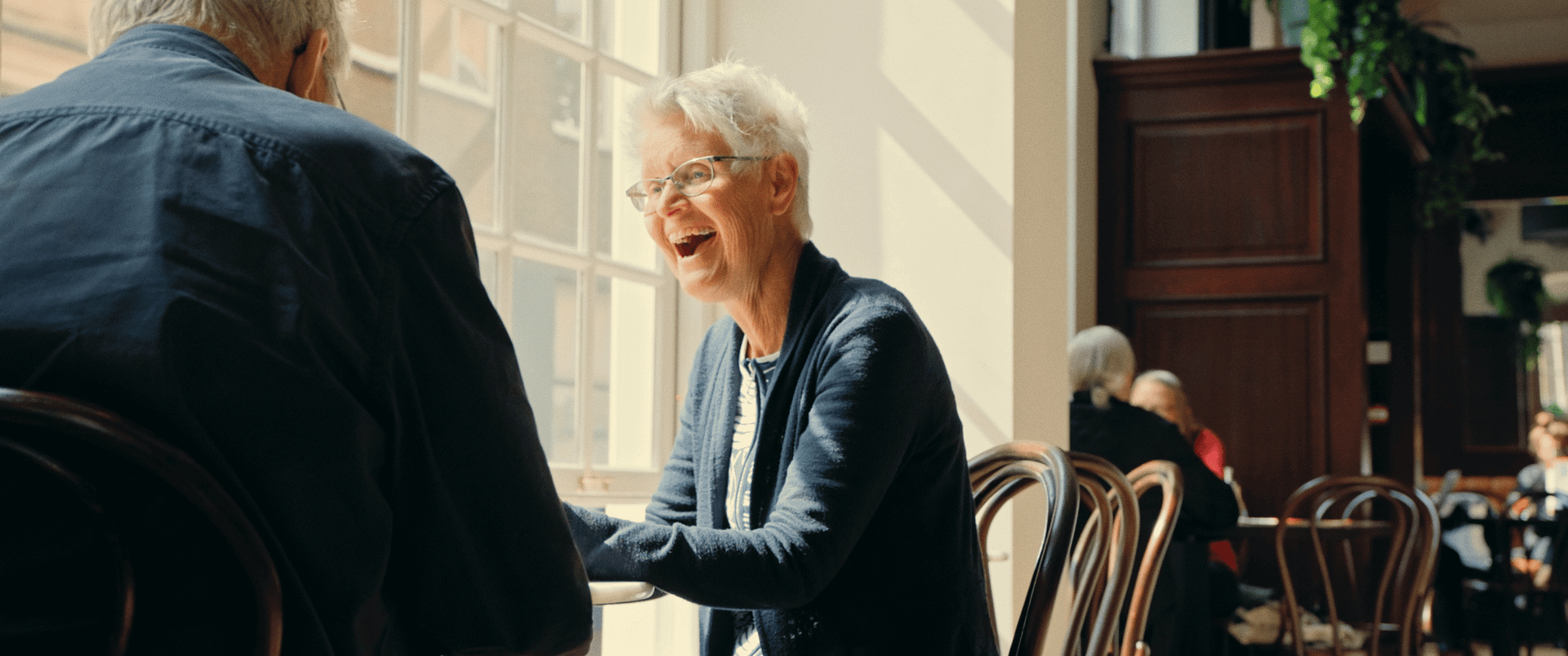 Older woman smiling during conversation in a bright cafe.