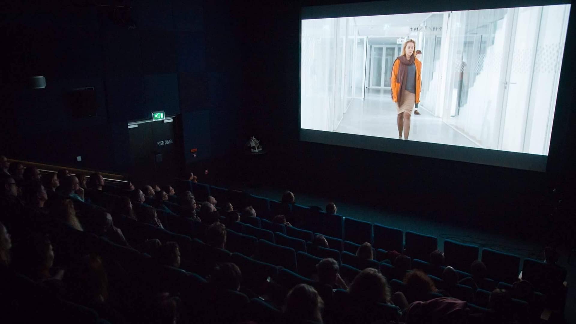 Audience watching a film screening in a dark cinema theater.
