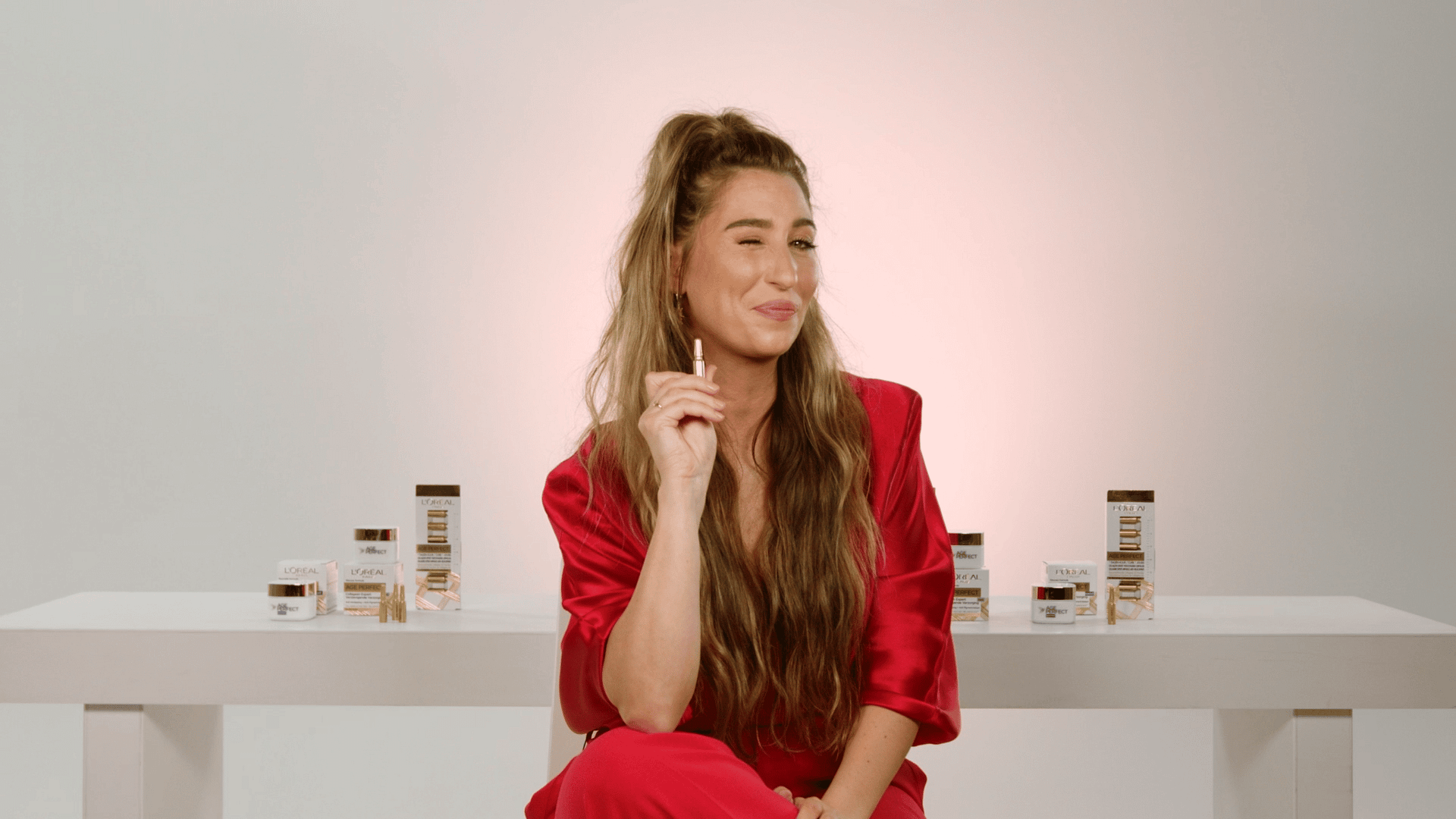 Woman in red blazer with long hair, smiling thoughtfully in a creative workspace.