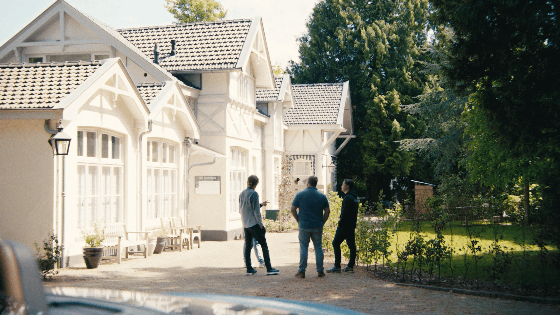 Three people standing outside modern white houses in a sunny neighborhood.