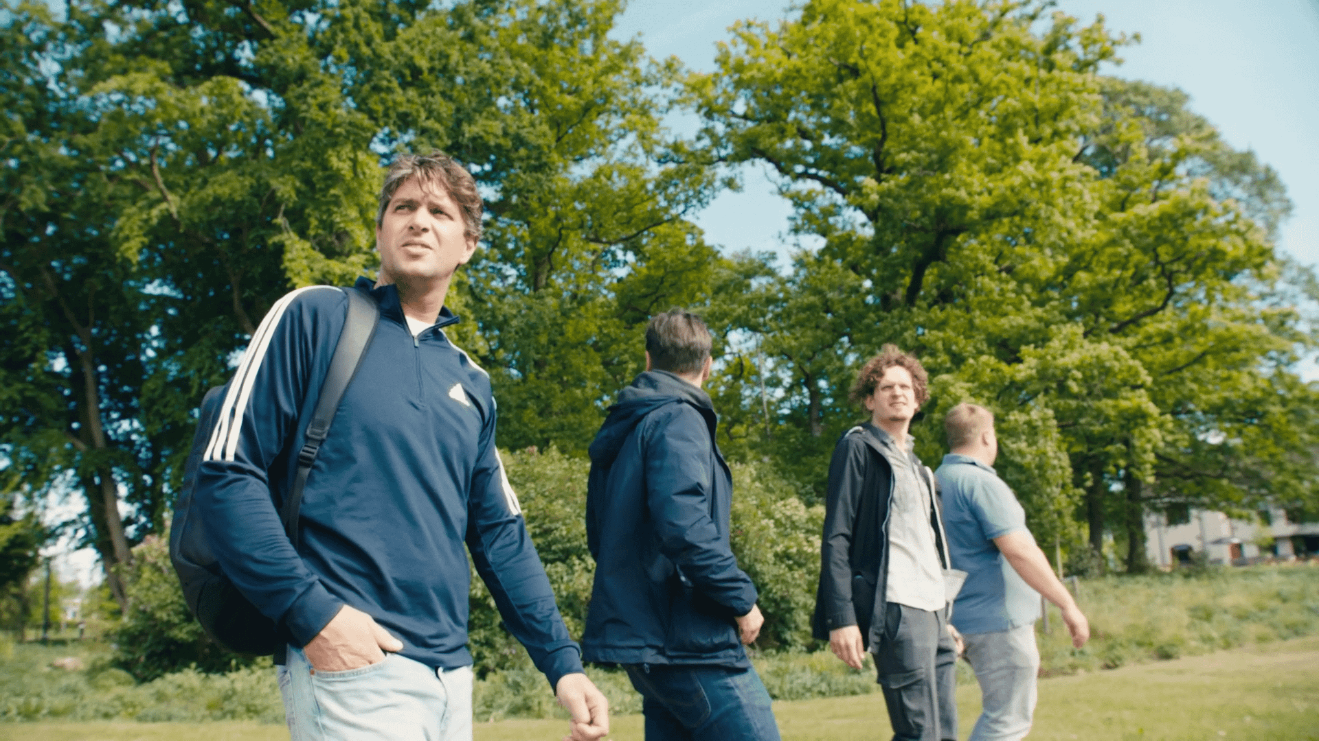 Group of young professionals walking outdoors in a park, discussing video projects.
