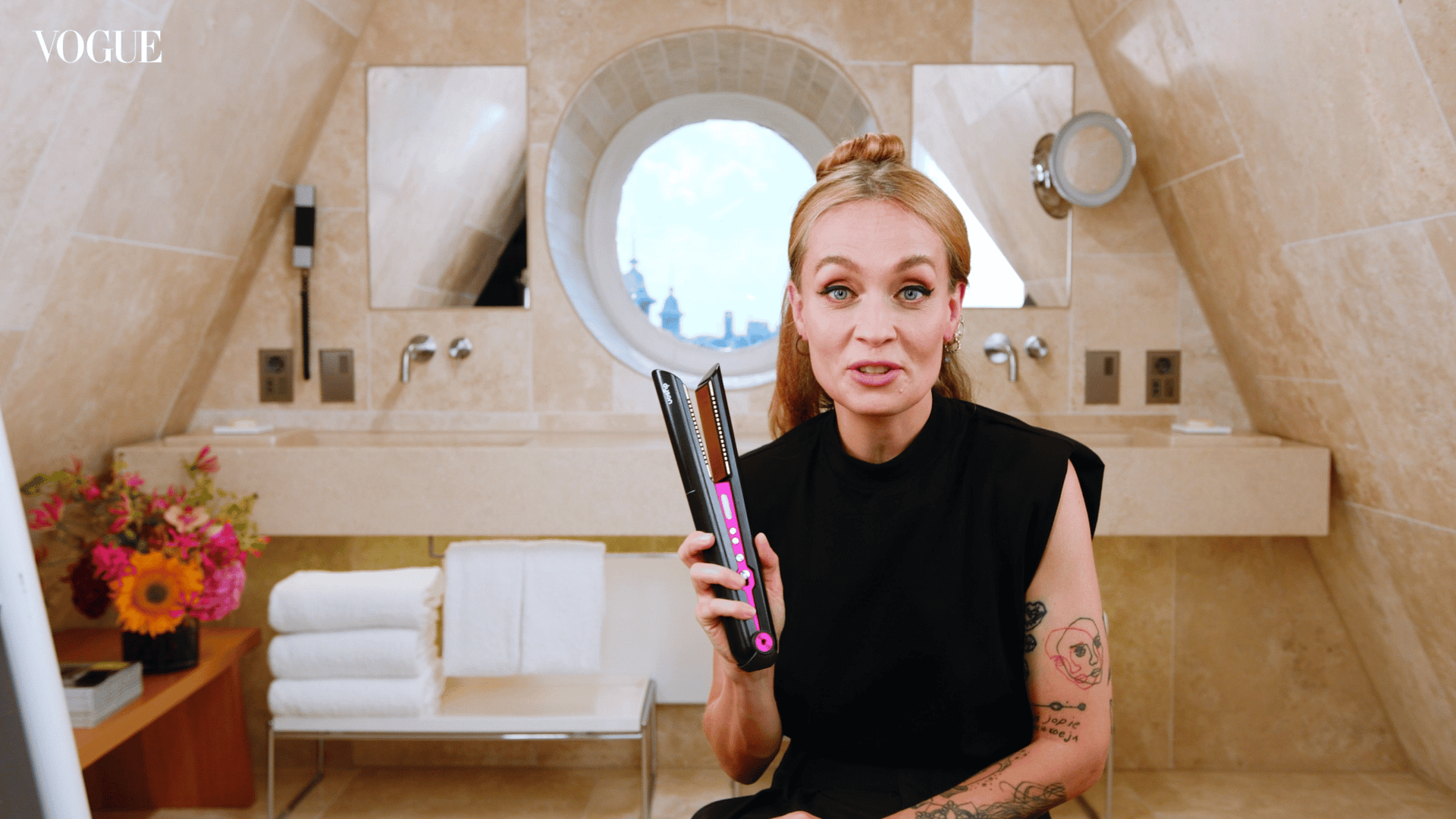Woman using a flat iron to style her hair in a stylish bathroom setting.