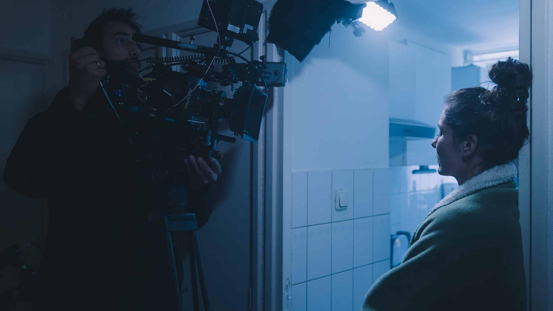 Filmmaker filming a woman in a dimly lit indoor setting for a video project.