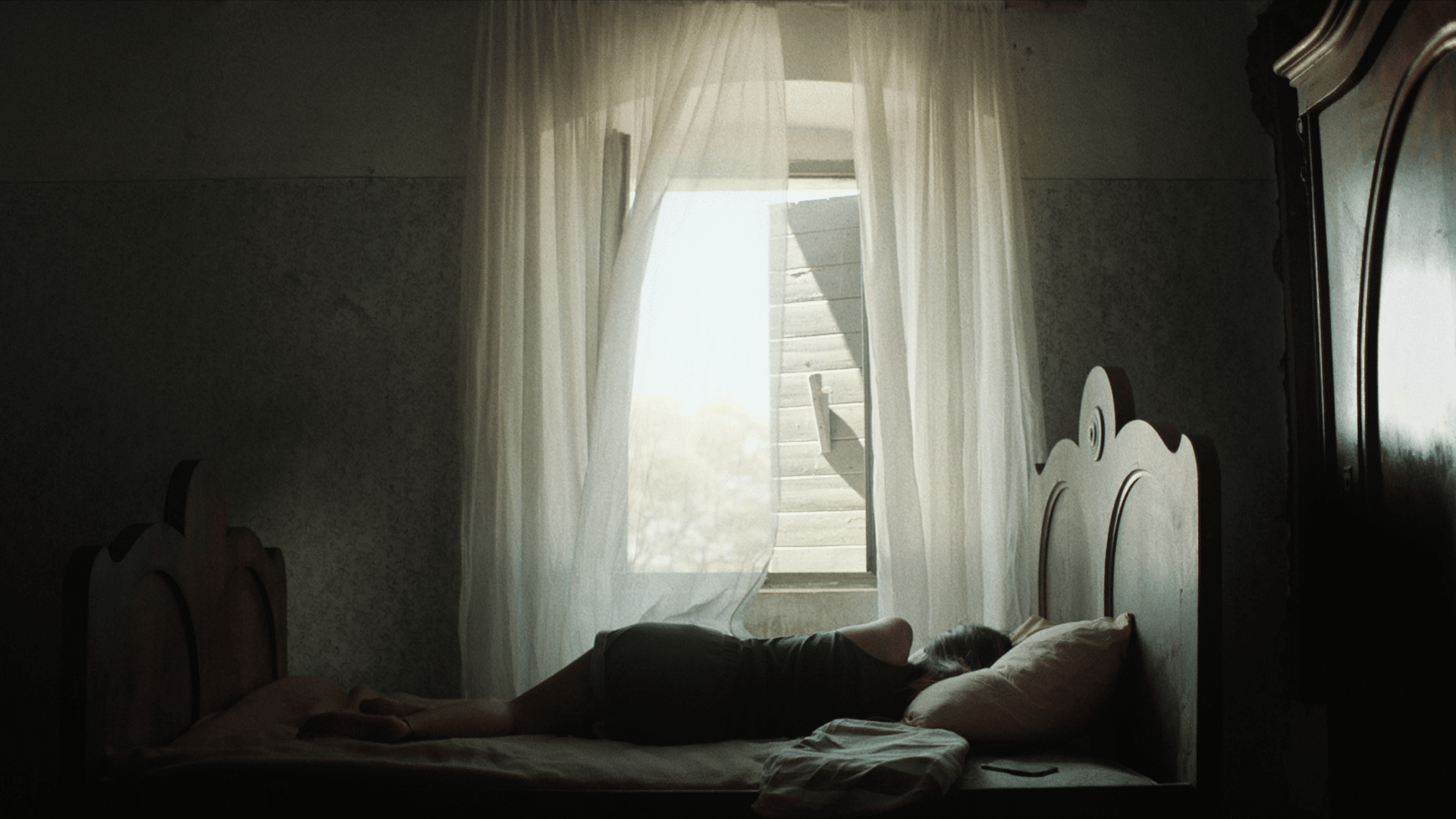 Person lying on bed with sunlight streaming through window, creative workspace scene.