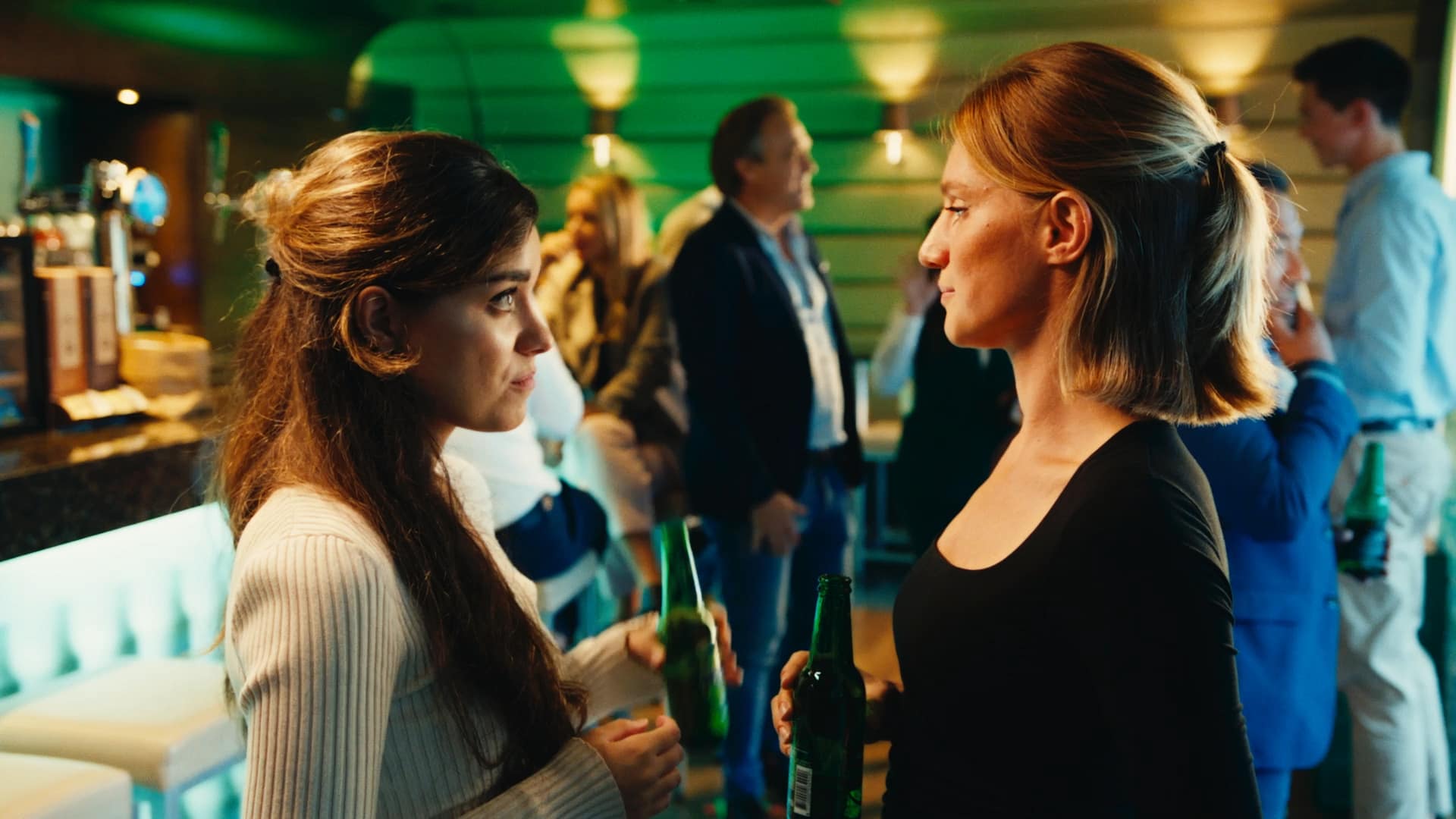 Two women conversing at a networking event with drinks, in a lively, colorful setting.