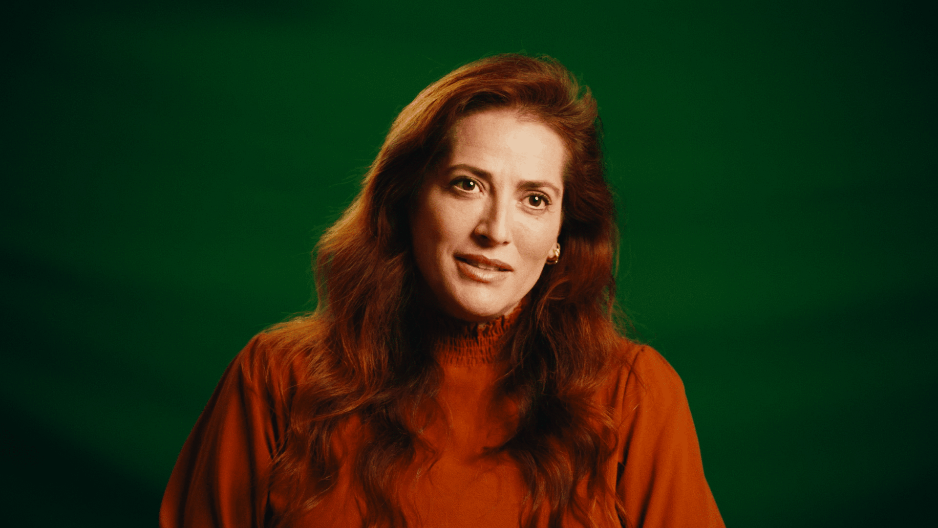 Professional woman with red hair in a burnt orange top against a green background.