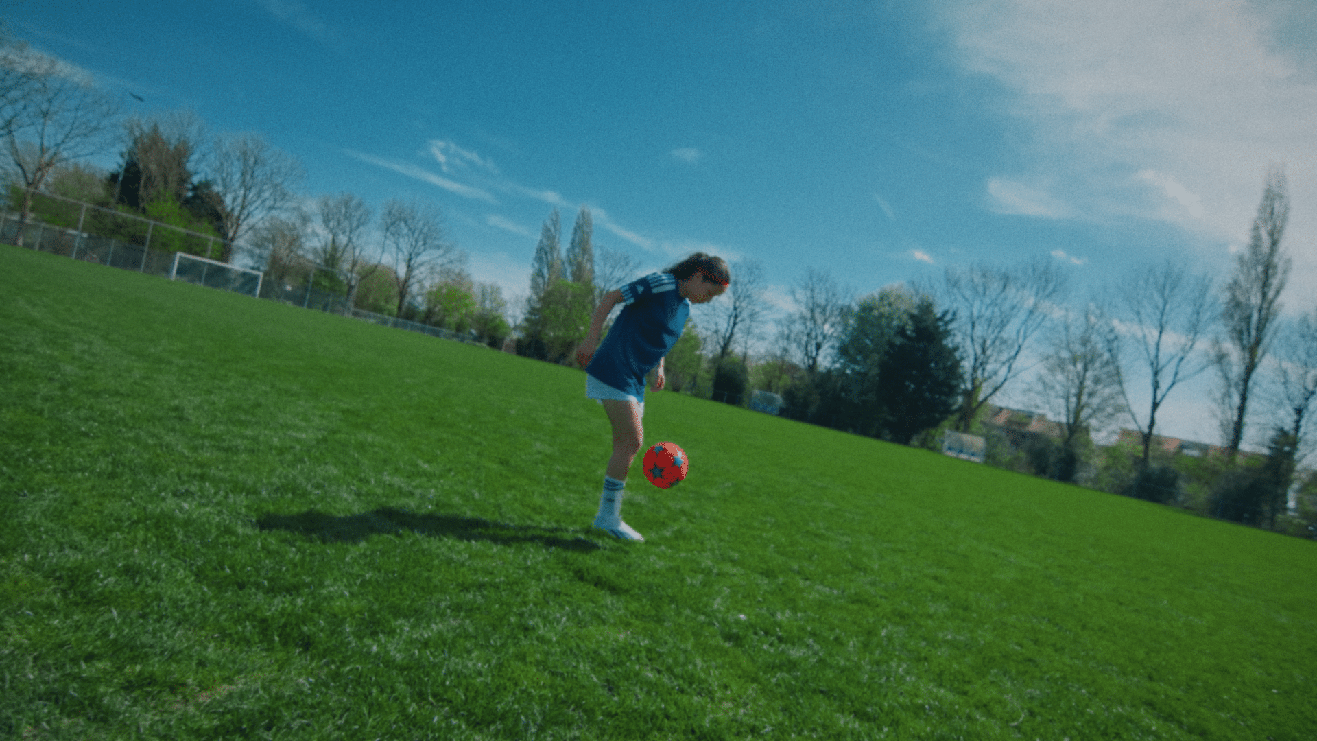 Young girl playing soccer outdoors on a sunny day.