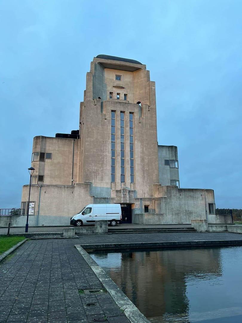 Modern concrete building with water feature in front, under a cloudy sky.