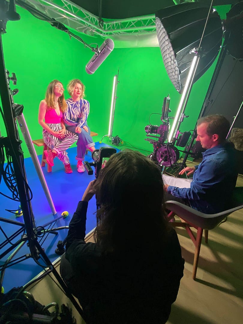 Green screen studio with crew filming two women for a creative video shoot.